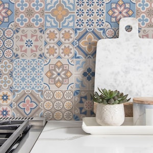 May include: A kitchen backsplash with a patterned tile design in shades of blue, brown, and pink. The tiles feature geometric shapes and floral motifs. A white cutting board, a succulent plant in a white pot, and a wooden tray with a white ceramic jar are on a countertop in front of the backsplash.