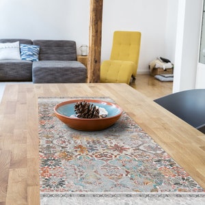 Puede incluir: Una mesa de comedor de madera con un acabado de madera clara. Un camino de mesa con estampado colorido se coloca sobre la mesa. Un tazón pequeño con una piña y conchas marinas se coloca sobre el camino de mesa.