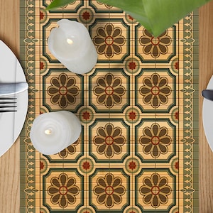 Puede incluir: Un camino de mesa con un patrón repetitivo de diseños florales verdes, marrones y rojos. El camino de mesa está sobre una mesa de madera con dos cubiertos, cada uno con un plato blanco, un tenedor y un cuchillo.