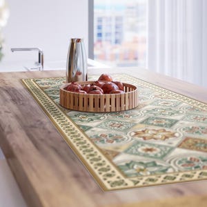 Könnte beinhalten: Ein Tischläufer mit geometrischem Muster in Grün-, Beige- und Brauntönen. Ein geflochtener Korb mit roten Granatäpfeln steht darauf. Eine silberne Kanne befindet sich ebenfalls auf dem Tisch.