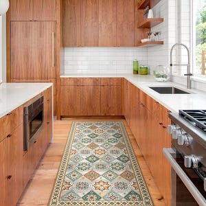 May include: A patterned kitchen runner rug with a repeating floral and geometric design in shades of green, orange, and cream. The rug is rectangular and placed on a wooden floor in a kitchen setting.