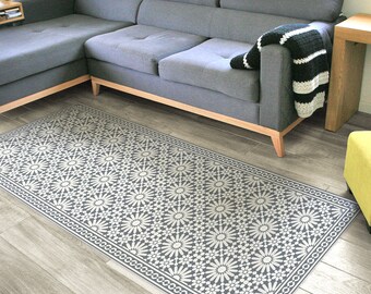 Puede incluir: Una alfombra de área gris y blanca con un diseño geométrico. La alfombra se coloca frente a un sofá seccional gris con una manta de tiro negra y blanca.
