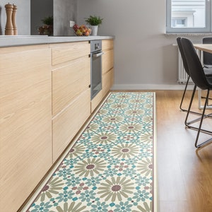 Op de afbeelding: Een keukenvloerkleed met een geometrisch patroon in tinten bruin, teal en cr&egrave;me. Het kleed ligt voor een houten keukeneiland met een oven van roestvrij staal.