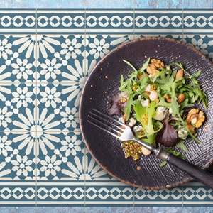 May include: A black plate with a salad of greens, blue cheese, walnuts, and almonds on a blue and white patterned placemat.