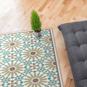 May include: A patterned rug with a geometric design in shades of beige, teal, and burgundy. The rug is on a hardwood floor with a small potted plant and a gray cushion.