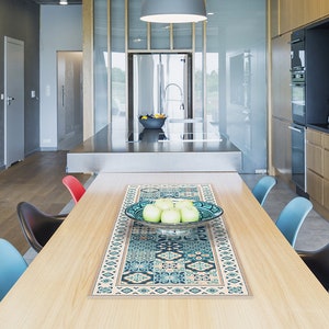Puede incluir: Un camino de mesa azul y beige con un borde decorativo. El camino de mesa está colocado sobre una mesa de madera con un cuenco de manzanas verdes en la parte superior.