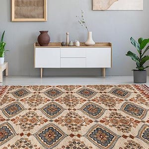May include: A large, rectangular area rug with an intricate geometric pattern in beige, brown, and blue. The rug features a central diamond motif surrounded by floral and geometric designs, with a dark brown border.