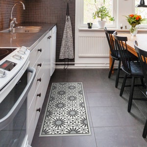 May include: A black and white patterned kitchen rug with a geometric design. The rug is placed in front of a white kitchen island with a black countertop and stainless steel appliances.