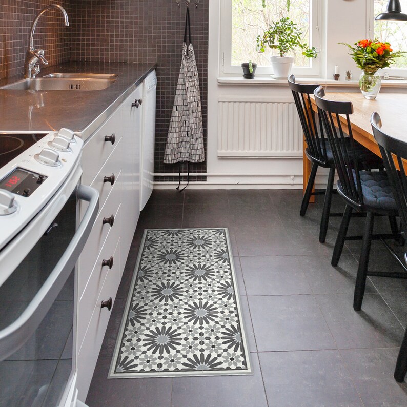 May include: A black and white patterned kitchen rug with a geometric design. The rug is placed in front of a white kitchen island with a black countertop and stainless steel appliances.