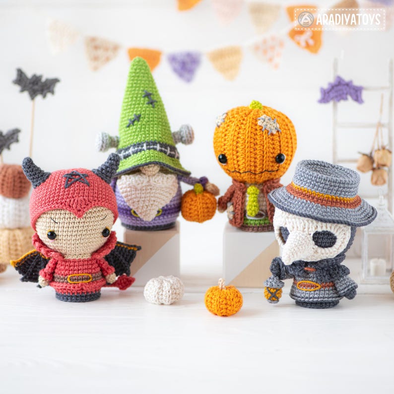 May include: Four crocheted dolls featuring a red devil with horns, a green gnome with a pointed hat, an orange pumpkin-headed figure, and a gray plague doctor with a beak mask. Each doll is crafted with yarn and includes small details.