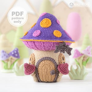 Może przedstawiać: Szydełkowy domek w kształcie grzyba z fioletowym kapeluszem ozdobionym pomarańczowymi i różowymi okręgami. Dom ma beżowy korpus, brązowe drzwi i różowe akcenty. Tekst "PDF pattern only" znajduje się w białym okręgu.