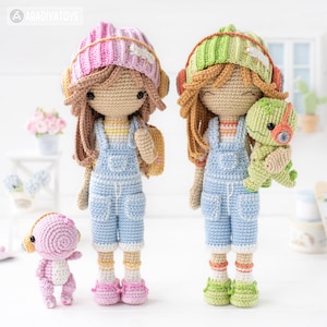 May include: Two crocheted dolls wearing overalls, hats, and headphones. The doll on the left is holding a pink crocheted dinosaur, and the doll on the right is holding a green crocheted dinosaur.