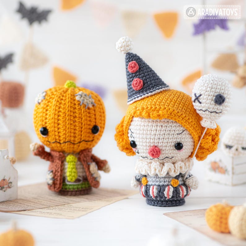 May include: Two handmade crochet dolls. One is a round orange pumpkin character with a brown jacket and green tie. The other is a clown figure with orange hair, a grey cone hat with red circles, a ruffled collar, and a white balloon with a face.