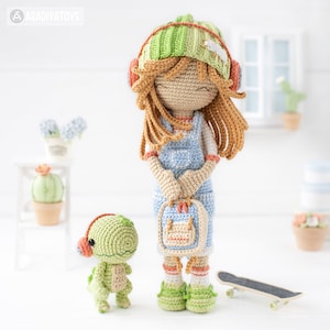 May include: A crocheted doll with brown hair wearing a green and white hat, blue overalls, and orange headphones. The doll is holding a small orange and blue backpack. A small green crocheted dinosaur with orange headphones is standing next to the doll. A skateboard is on the floor in front of the doll.