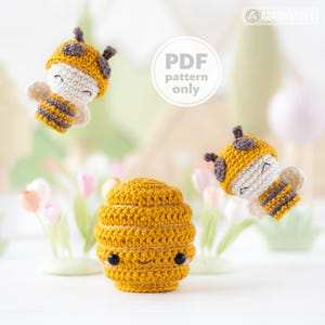 May include: A crocheted yellow beehive with a smiling face and two crocheted bees. The bees have yellow and grey striped bodies, white wings, and yellow hats. The text "PDF pattern only" is in a white circle.