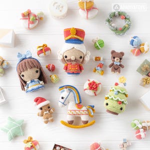 Op de afbeelding: Een verzameling handgemaakte gehaakte speelgoed, waaronder een notenkraker, een pop, een schommelpaard, een teddybeer en een kerstboom. Het speelgoed is in verschillende kleuren, zoals rood, blauw, groen en wit. Het speelgoed is op een wit oppervlak geplaatst.