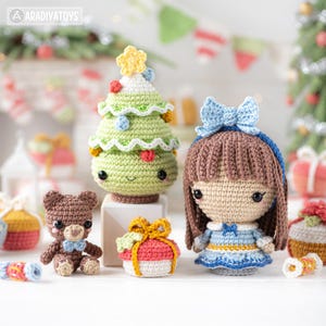 Op de afbeelding: Een verzameling handgemaakte gehaakte kerstversieringen en poppen. Bevat een groene kerstboom met een gele ster, een bruine teddybeer, een pop met een blauwe strik en een geschenkdoos. De versieringen zijn in verschillende kleuren en ontwerpen.