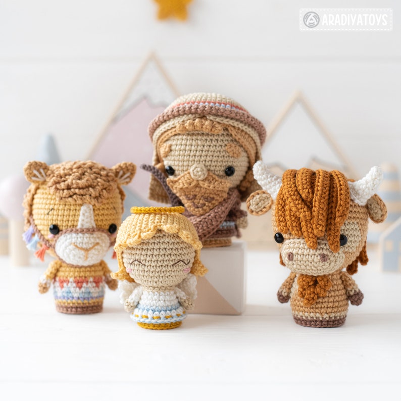 May include: A set of four crocheted amigurumi toys, including a shepherd, an angel, a camel, and a cow. The toys are all brown and beige with colourful accents. The toys are arranged on a white surface.