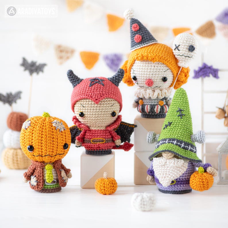 May include: A collection of four crocheted dolls featuring a pumpkin-headed figure, a red devil with wings, a clown with a white balloon, and a green-hatted gnome. Each doll is crafted with detailed yarn textures, vibrant colors, and small accessories.