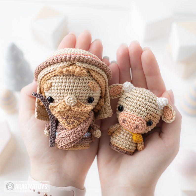 May include: A crocheted shepherd figurine with a brown staff and a crocheted cow figurine with a yellow scarf. Both figurines are brown and beige.