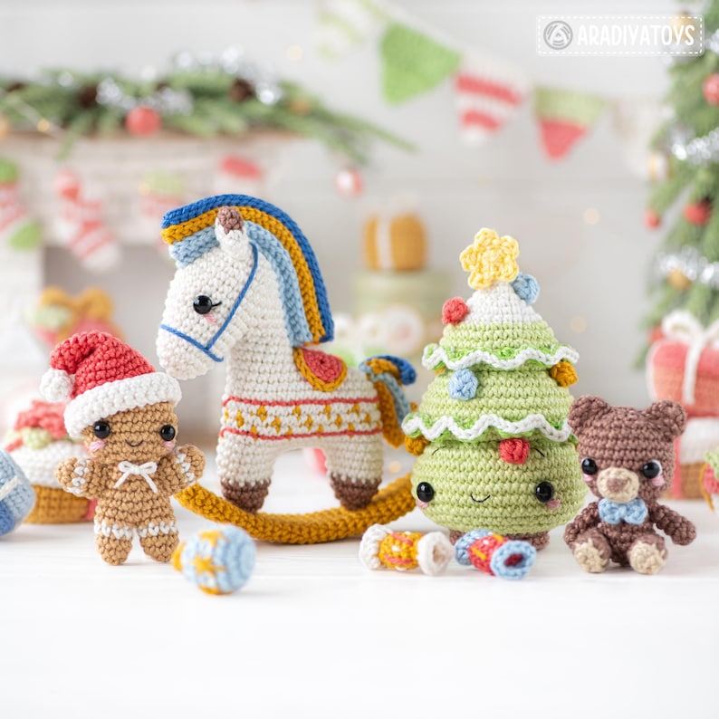 Op de afbeelding: Een verzameling handgemaakte gehaakte kerstversieringen. Bevat een wit schommelpaard met een blauwe en gele manen, een peperkoekmannetje met een kerstmuts, een groene kerstboom en een bruine teddybeer met een blauwe strik.