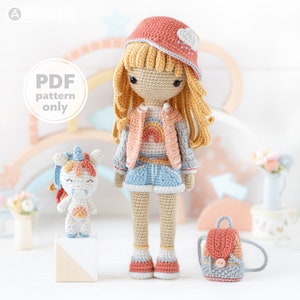 Può includere: Bambola all'uncinetto con lunghi capelli biondi, indossa una giacca rosa, pantaloncini blu e un cappello abbinato. Sono presenti anche un piccolo unicorno e uno zaino all'uncinetto. Il testo "PDF pattern only" è visibile.