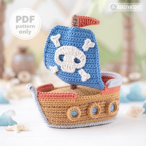 May include: A crocheted pirate ship toy. The blue sail has a white skull and crossbones. The ship's body is tan with orange and blue details. The text "PDF pattern only" is in a white circle.