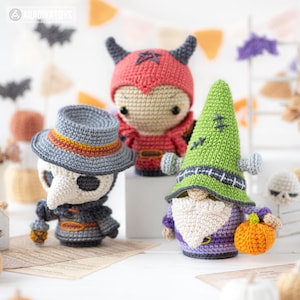 May include: Three crocheted dolls featuring a plague doctor in a grey hat, a red horned character, and a green-hatted gnome with a white beard holding an orange pumpkin. Each figure is crafted with detailed yarn stitching and distinct features.