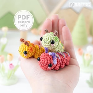 May include: Three small crocheted caterpillar toys in yellow, green, and red, each featuring black bead eyes, pink stitched cheeks, and small antennae. A circular white graphic overlay in the top left corner displays the text PDF pattern only.