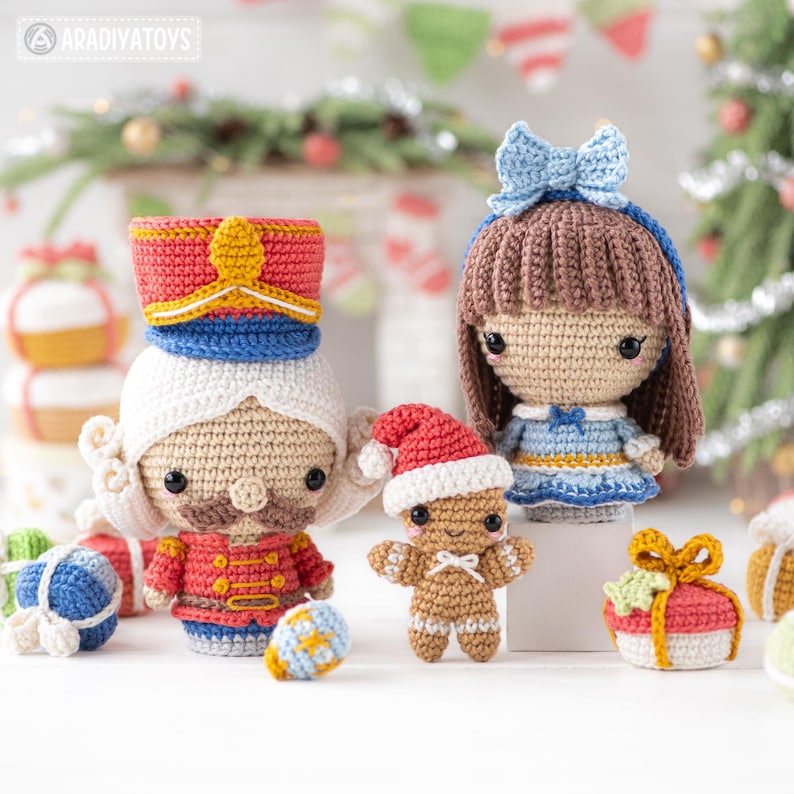 Op de afbeelding: Een verzameling handgemaakte gehaakte kerstversieringen. De set bevat een notenkraker, een poppenmeisje, een peperkoeken man en ingepakte geschenkdozen. De notenkraker draagt een rode en blauwe hoed. Het poppenmeisje heeft een blauwe strik. De peperkoeken man draagt een kerstmuts.