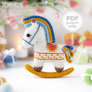May include: A crocheted rocking horse in white with blue, yellow, and brown details. The horse has a colourful mane and tail, and a decorative saddle. The text "PDF pattern only" is visible in a white circle.