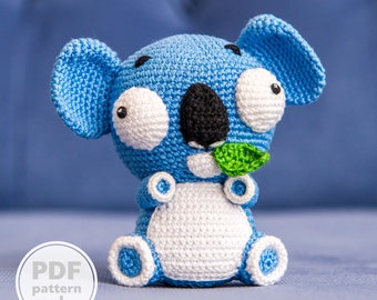 May include: A crocheted blue and white koala holding a green leaf. The koala has large, white eyes and a black nose. The koala is sitting on a blue surface. PDF pattern only.