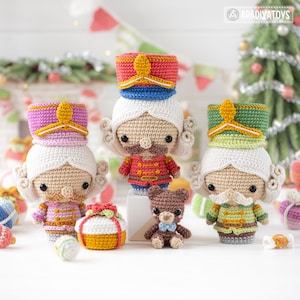Op de afbeelding: Een verzameling handgemaakte gehaakte kerstversieringen, waaronder drie notenkrakerfiguren met witte pruiken en kleurrijke uniformen, een kleine teddybeer en een geschenkdoos. De ornamenten zijn in tinten rood, groen, roze en goud.