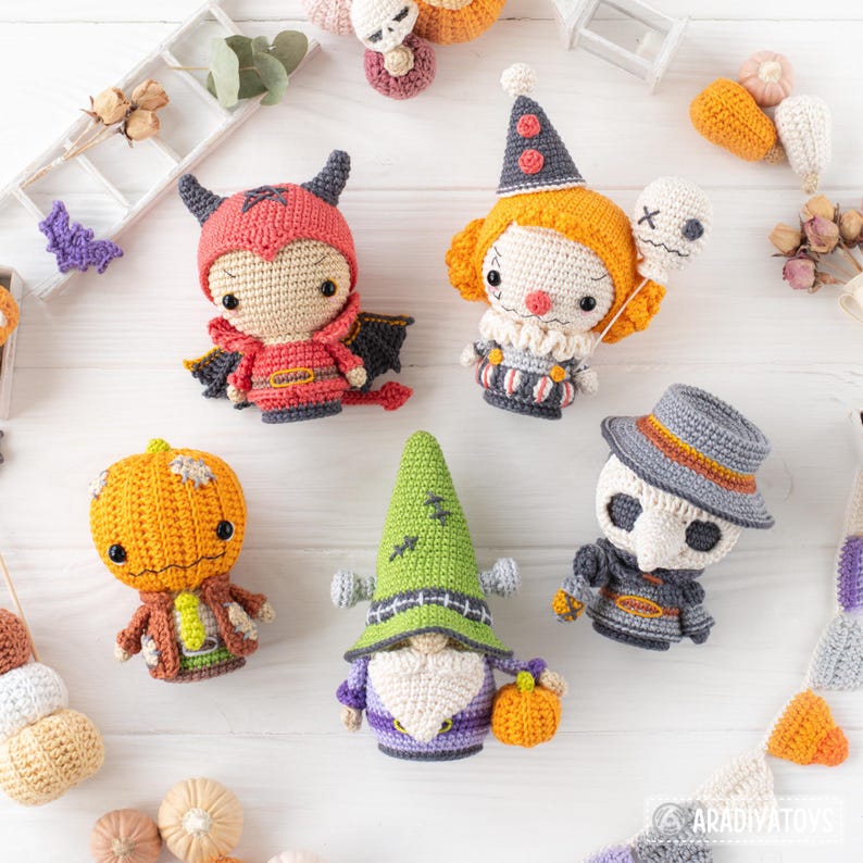 May include: A collection of five crocheted dolls featuring a red devil, a clown with a balloon, a pumpkin-headed figure, a green-hatted gnome, and a plague doctor. Each doll is crafted with intricate yarn details and distinct character features.