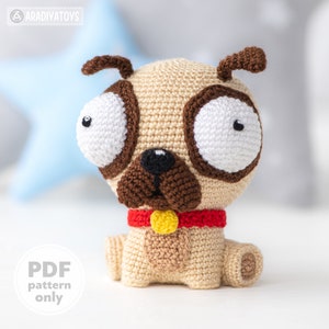 May include: A crocheted pug dog toy with large white eyes, a brown nose, and a red collar with a yellow tag. The toy is sitting on a white surface.