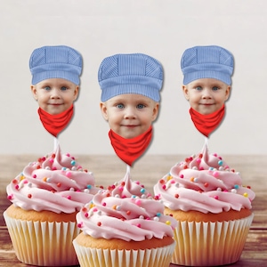 May include: Three pink cupcakes with colorful sprinkles topped with blue and white striped engineer hats and red bandanas. The hats have a child's face printed on them.