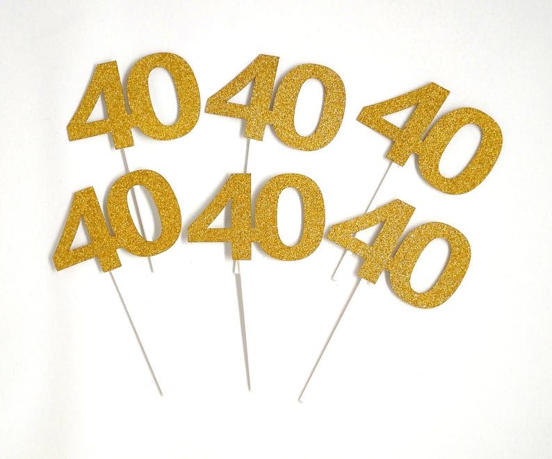 May include: Six gold glitter cake toppers, each with the number "40" printed on it. The toppers are on white sticks.