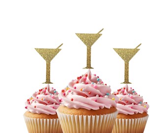 May include: Three pink cupcakes with gold glitter martini glass toppers. The cupcakes are decorated with colorful sprinkles.