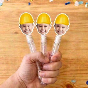 May include: Three clear plastic bubble wands, each topped with a cutout of a smiling child wearing a bright yellow construction hard hat. The wands feature a cylindrical design and are held together in a cluster, showcasing the custom face toppers.