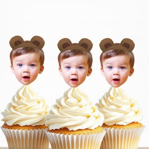May include: Three cupcakes with white frosting and brown bear ears on top. Each cupcake has a different child's face on top.