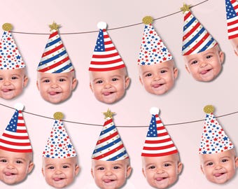 May include: A decorative party banner featuring multiple cutouts of a baby face wearing various cone-shaped party hats. The hats display red, white, and blue patterns including American flag stripes and star prints, topped with gold or white pom-poms.