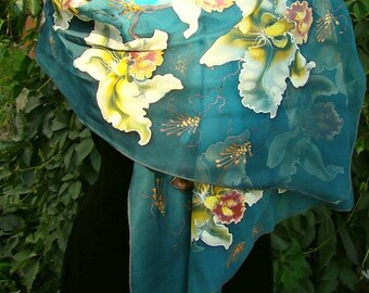 Puede incluir: Una bufanda de seda azul turquesa con flores de orquídea blancas y amarillas pintadas a mano. La bufanda está drapeada sobre un vestido negro.
