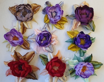 May include: Nine handmade fabric flowers with different colors and textures. The flowers are made with silk ribbon and have a variety of colors, including purple, red, and brown.