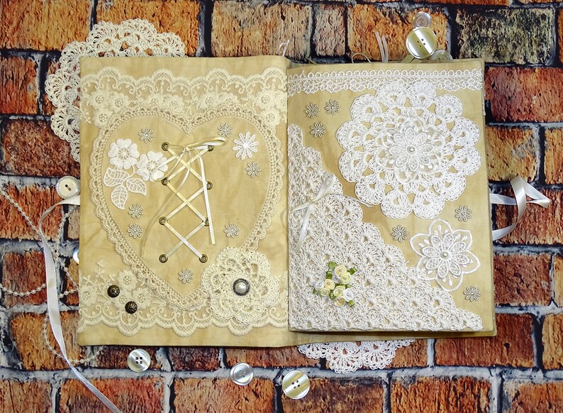 May include: A handmade journal with a brown cover decorated with white lace, crocheted doilies, and a heart-shaped design with a white ribbon and lace. The journal is closed and lying on a brick surface.