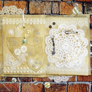 May include: A handmade journal with a brown paper cover decorated with lace, buttons, and a crocheted doily. The journal has a heart-shaped pocket on the front cover.
