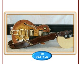 May include: A brown leather guitar strap with a decorative pattern. The strap is resting on a guitar and a guitar case. The image includes the text "the Leather Pattern Store" and "Ergonomic Guitar Strap".