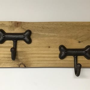 May include: A wooden dog lead rack with two bone-shaped hooks. The rack is made of natural wood and has a rustic look.