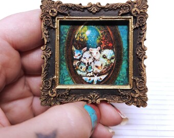 May include: A small, framed artwork with a whimsical scene of animal-like creatures. The artwork is set within an ornate, dark brown frame with gold accents. The image depicts a group of animals in a forest setting, with a blue and green colour palette.