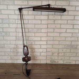 May include: A brown metal desk lamp with a long, adjustable arm and a rectangular light fixture. The lamp is mounted on a base with a curved foot.