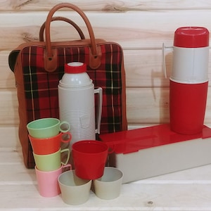 May include: A vintage picnic set with a plaid bag, two thermoses, and six plastic cups in various colors. The thermoses are red and white, and the cups are green, orange, yellow, pink, and beige.
